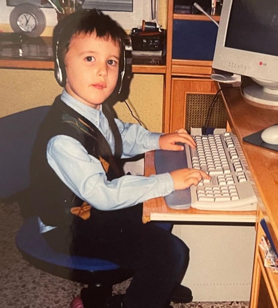 Javi de niño, con uniforme del colegio, sentado ante un ordenador